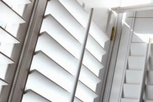 Close-up of white plantation shutters with slanting louvers arranged in parallel rows, letting in some light. Emphasizing geometric patterns and a bright, airy atmosphere, this image showcases impeccable shutter installation in Tarrant County.