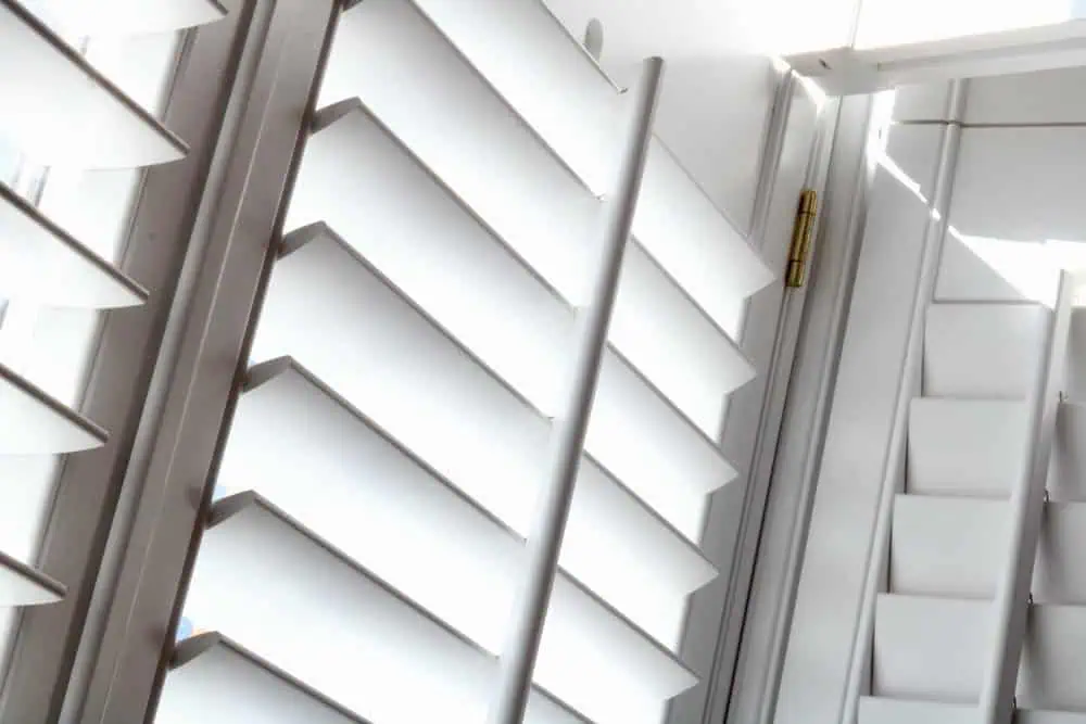 Close-up of white plantation shutters with slanting louvers arranged in parallel rows, letting in some light. Emphasizing geometric patterns and a bright, airy atmosphere, this image showcases impeccable shutter installation in Tarrant County.