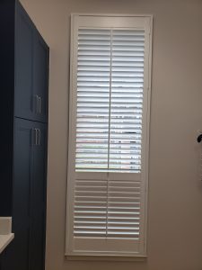 A tall window with white horizontal blinds partially open, allowing light to filter through, illuminates the room like our 'About Us' page highlights our story. To the left, a dark cabinetry unit with closed doors is visible against a wall painted a soft neutral color.
