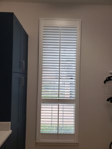 A tall window with white blinds partially open, letting in a soft haze of natural light. To the left, a blue cabinet with silver handles stands proud. On the right, a wall-mounted drying rack partially appears—just a glimpse into the world behind our "About Us" story.
