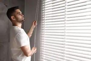 Bright white window blinds being adjusted by a man in a modern interior space.