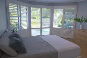 Elegant white plantation shutters on large bay window in bedroom with natural light.