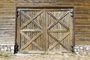 Rustic wooden barn doors with crossbuck design mounted on a weathered wood exterior wall